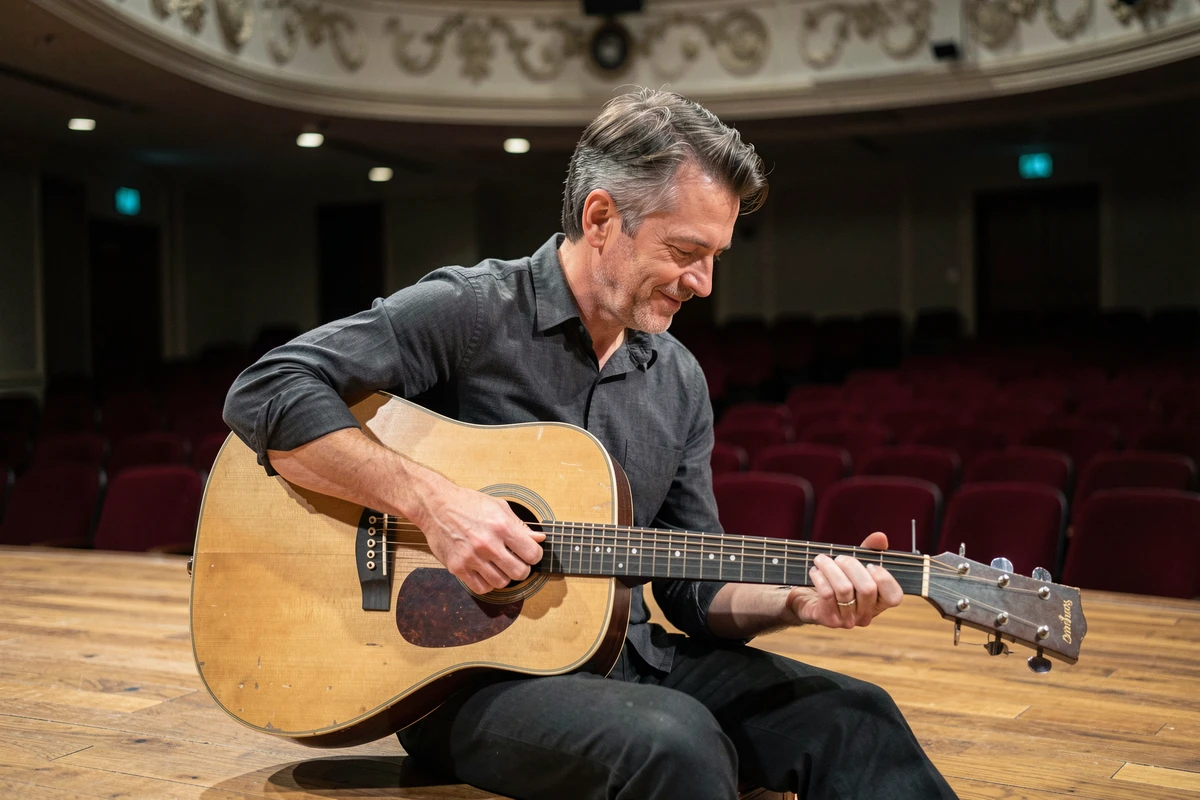 Chanteur masculin assis sur scène avec une guitare acoustique dans une salle de concert intimiste, représentant les artistes musicaux majeurs à découvrir